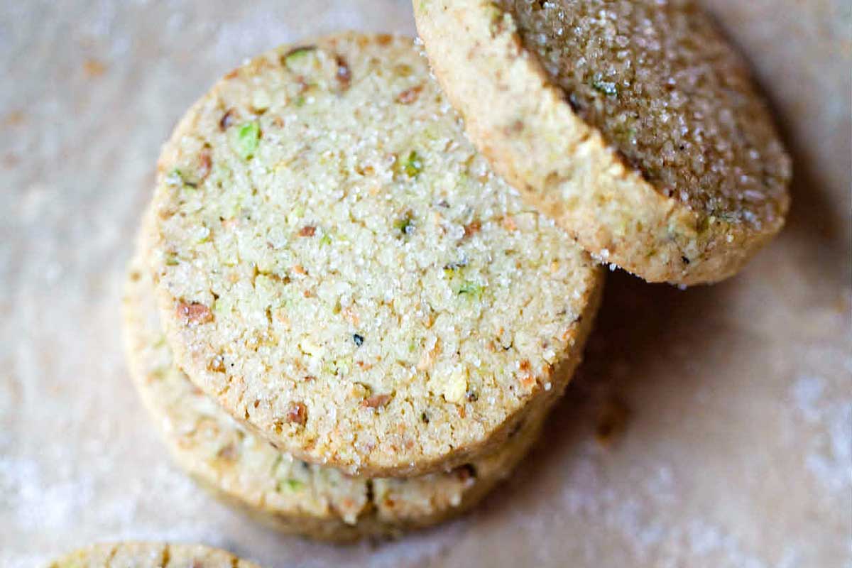 Five round pistachio shortbread cookies with a few broken pistachios on the side