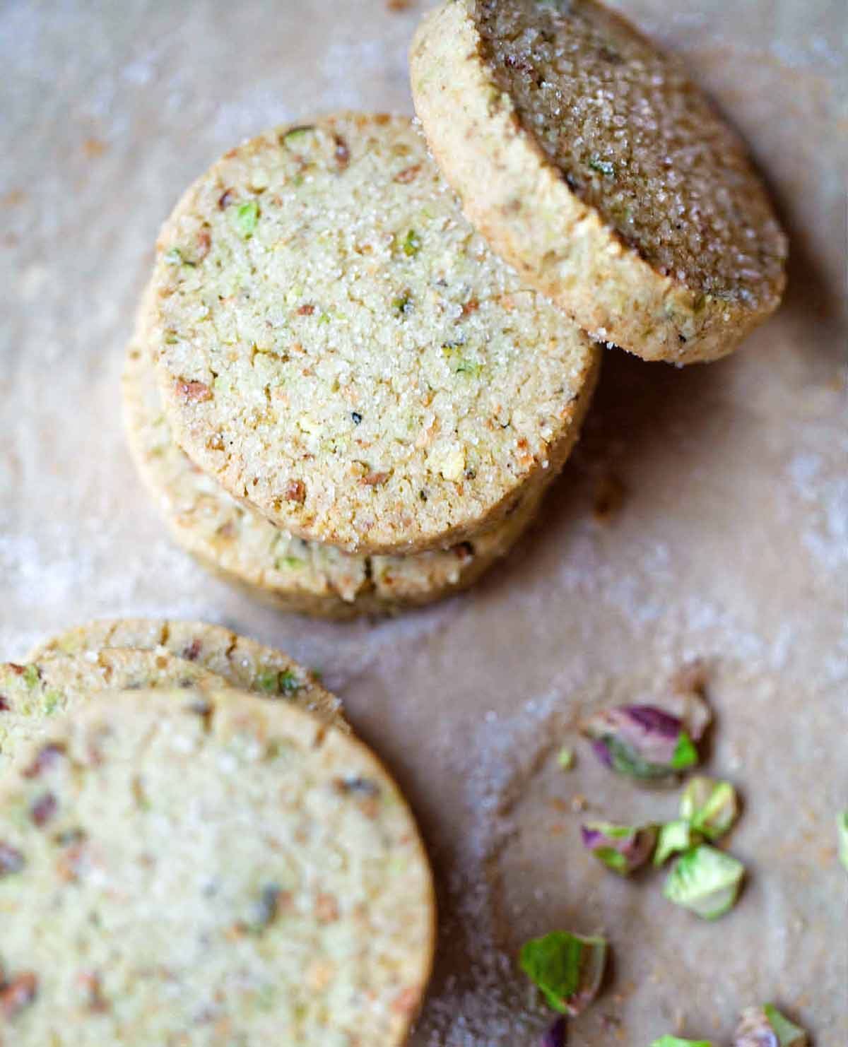 Five round pistachio shortbread cookies with a few broken pistachios on the side