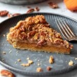 A slice of pumpkin pecan pie on a plate with the remainder of the pie in the background.