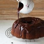 Chocolate ganache being poured over a chocolate Bundt cake that is on a wire stand