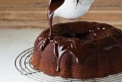 Chocolate ganache being poured over a chocolate Bundt cake that is on a wire stand