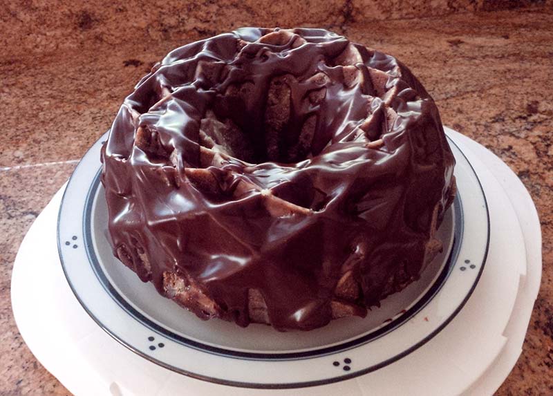 A chocolate jubilee Bundt cake topped with chocolate ganache sitting on a white plate