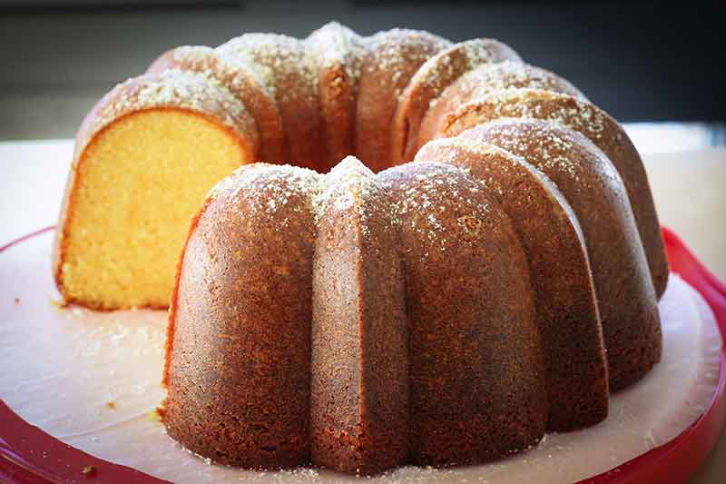 A orange olive oil Bundt cake with a slice removed sitting on a red cake plate