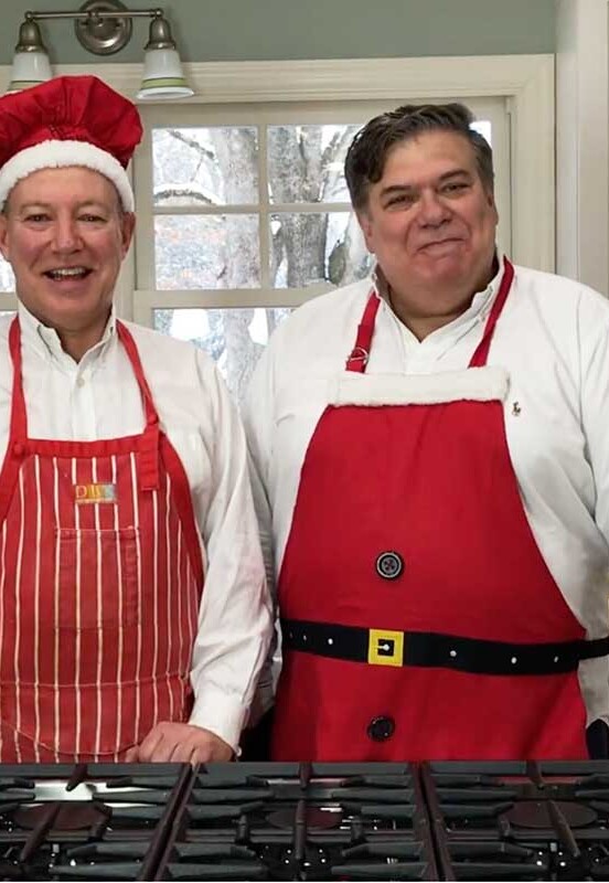 The One in a red apron and red chef's hat and David Leite in a Santa apron in their kitchen