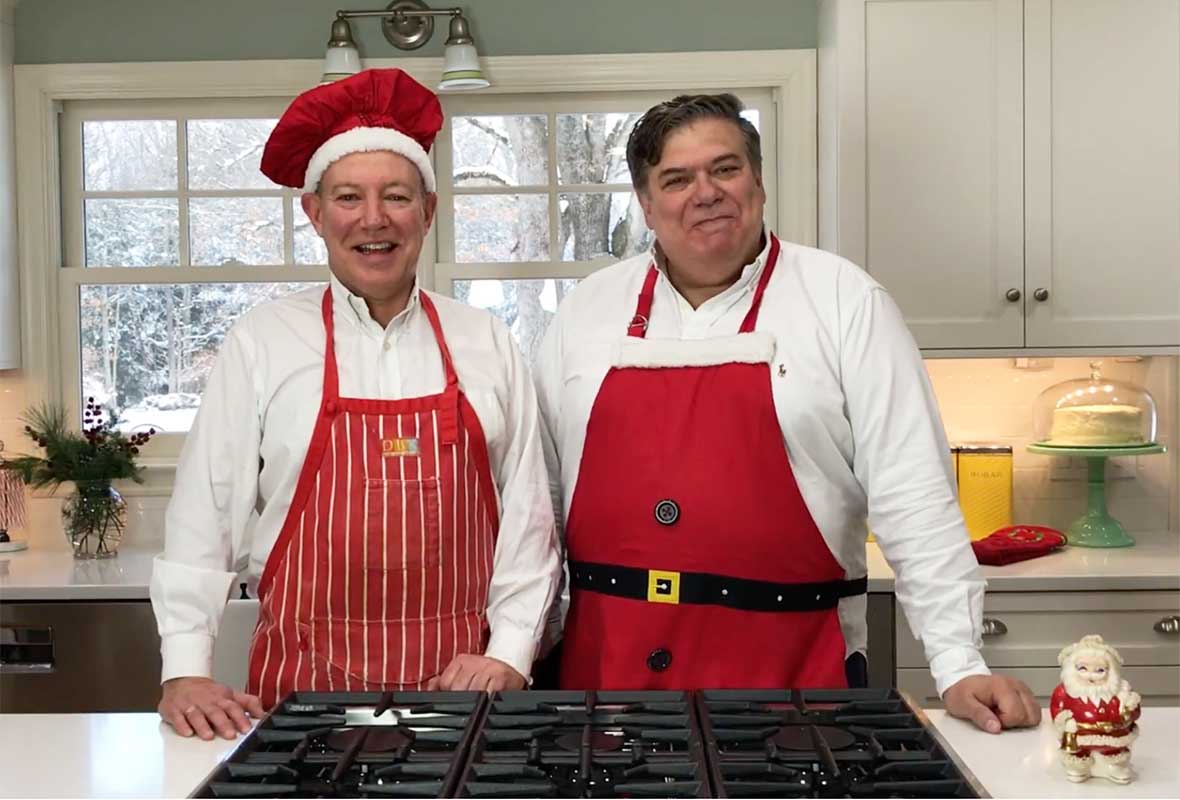 The One in a red apron and red chef's hat and David Leite in a Santa apron in their kitchen