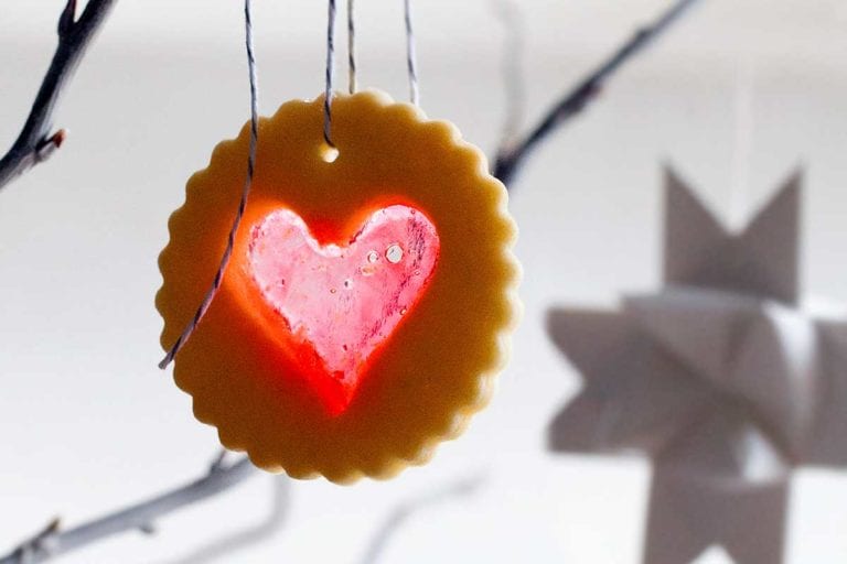 A scalloped round sugar cookie with a heart-shaped windowpane cutout hanging from a tree branch.