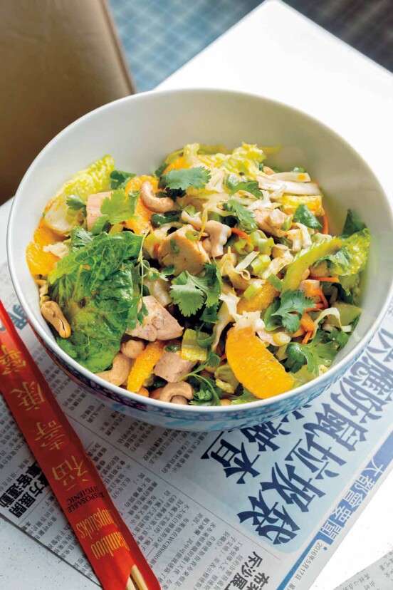 A bowl filled with Chinese chicken salad--greens, chicken, cilantro, and mandarin orange segments with chopsticks on the side