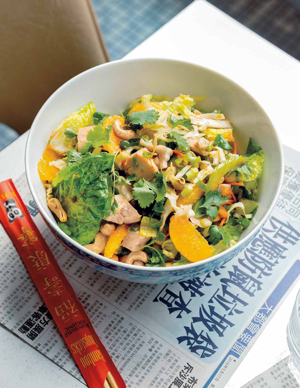 A bowl filled with Chinese chicken salad--greens, chicken, cilantro, and mandarin orange segments with chopsticks on the side
