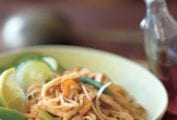 Pad Thai noodles, crunchy noodles. cucumber, bean sprouts, and lime wedges in a bowl, a bottle of chile-vinegar