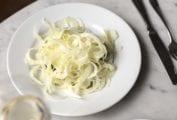 White plate of shaved fennel salad with provolone cheese, and a glass of white wine.