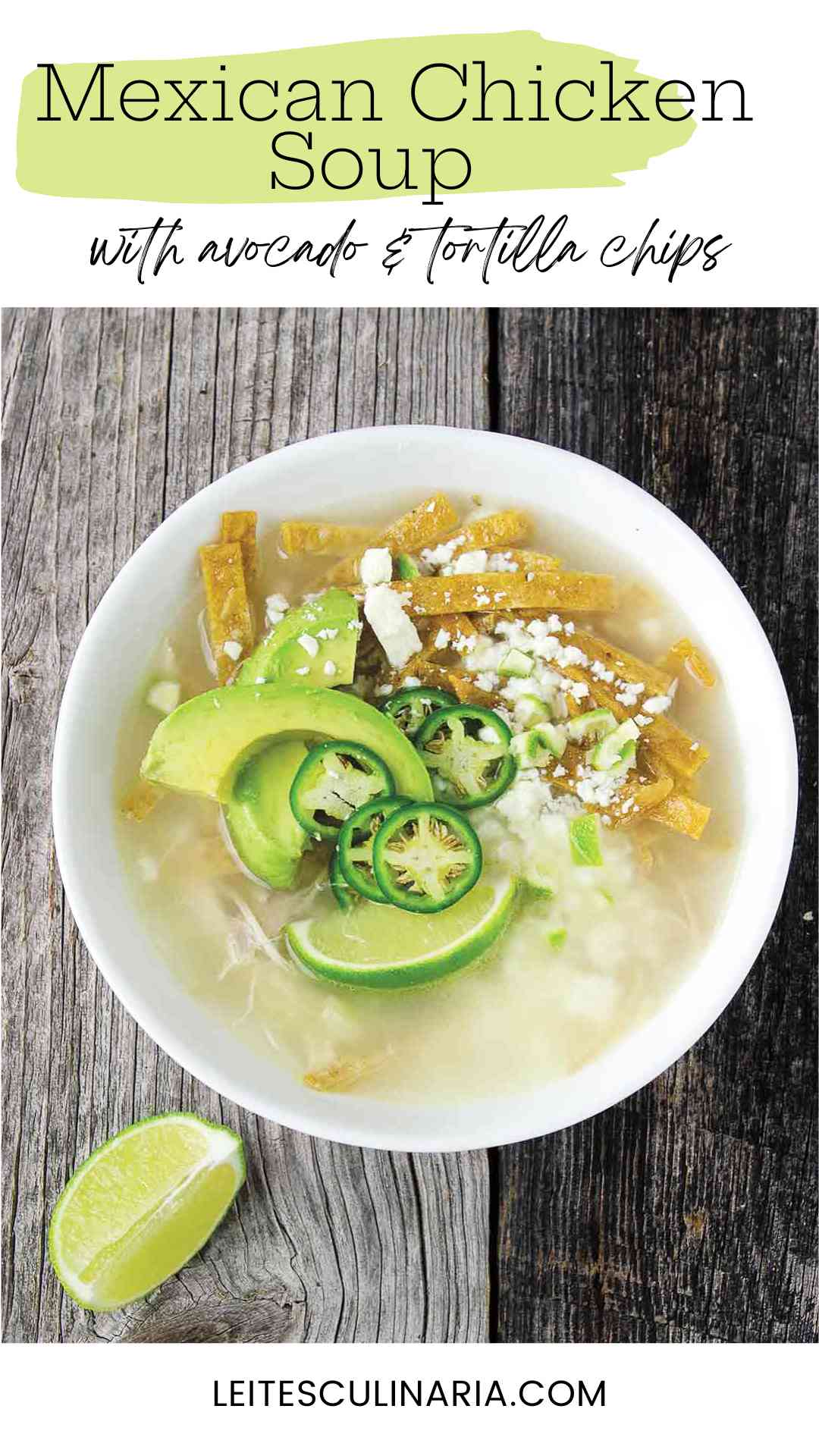 A white bowl filled with broth, avocado slices, lime wedges, cheese, and tortilla strips.