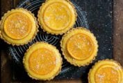 Five small tarts filled with orange curd and topped with candied orange slices on a cooling rack