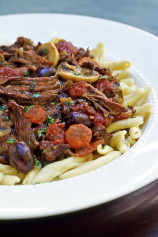 A white bowl filled with French beef stew piled atop pasta.