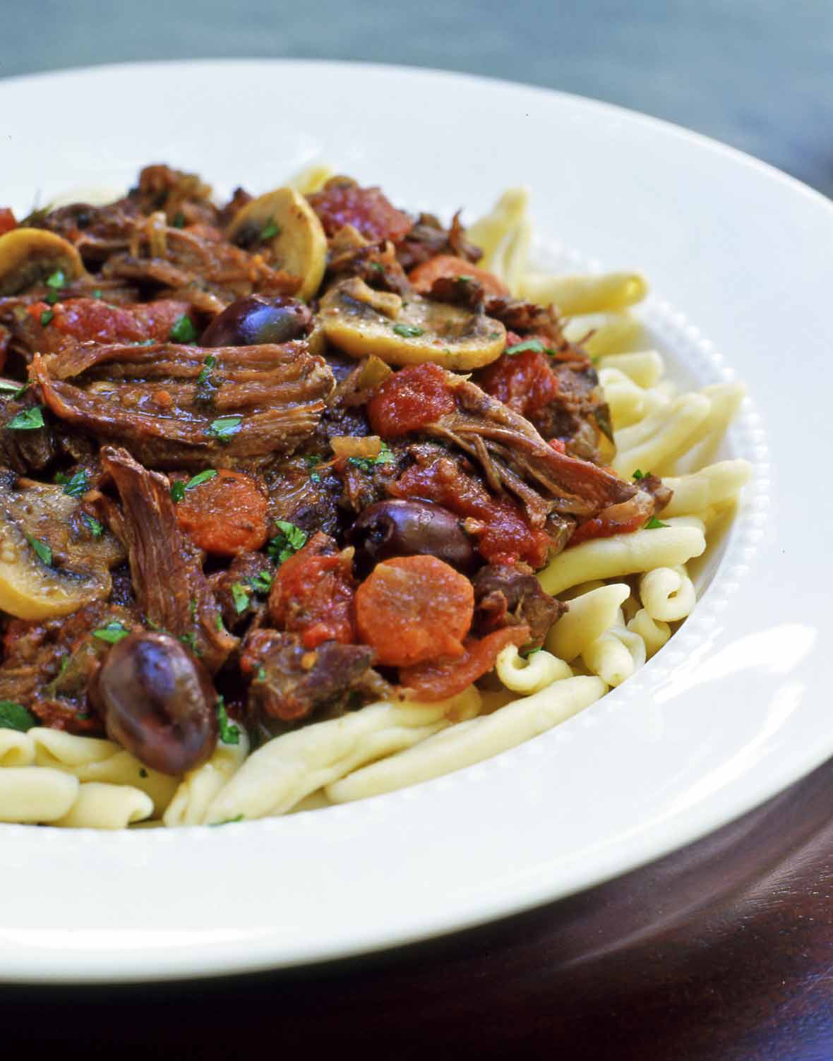 A white bowl filled with French beef stew piled atop pasta.