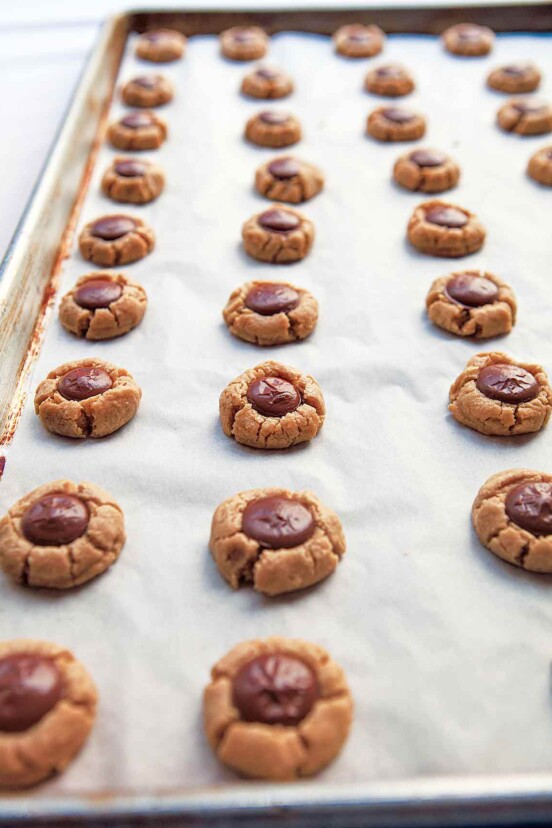 A parchment lined baking sheet filled with rows of round peanut butter cookies with chocolate centers.