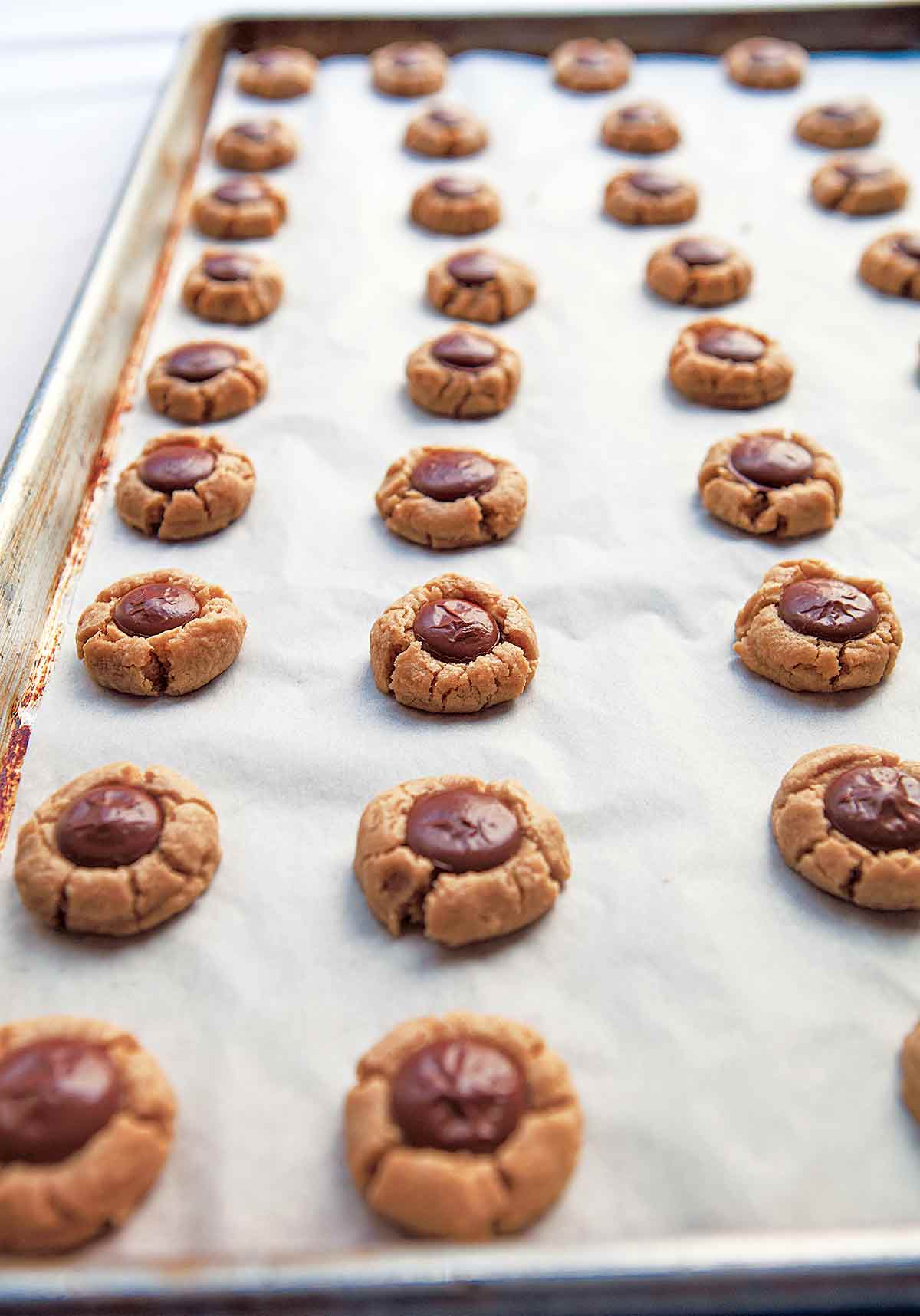 A parchment lined baking sheet filled with rows of round peanut butter cookies with chocolate centers.