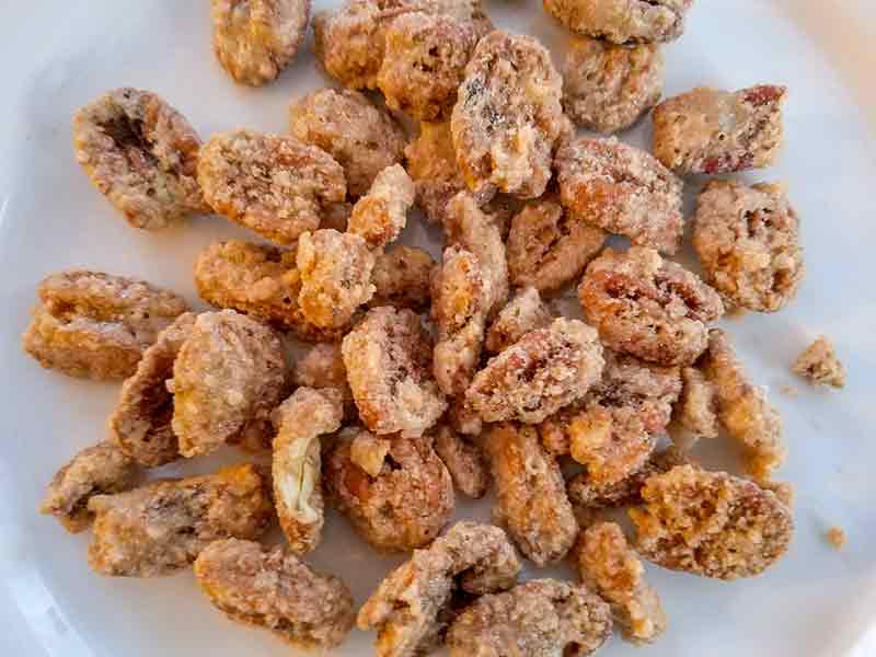 A white plate with a mound of coated and crispy candied pecans