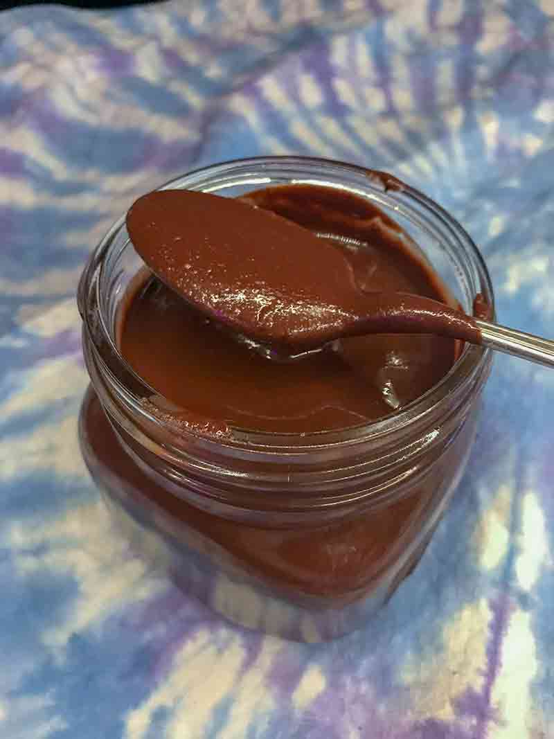 A glass jar of silky homemade Nutella, resting on top is a spoon with Nutella