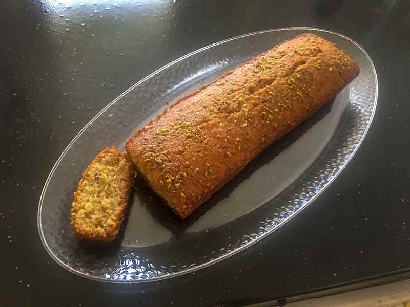 A long pistachio pound cake, with one slice cut, all on an oval silver platter