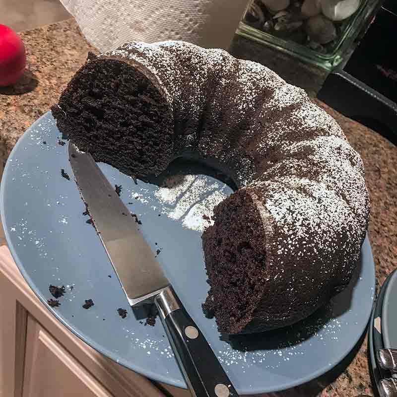 Three-quarters of a chocolate Bundt cake with powdered sugar on top sitting on a blue plate