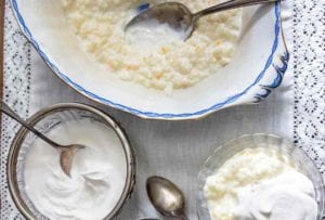 Serving bowl and small bowl of French rice pudding topped with whipped cream, along with spoons on a lace tablecloth