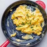 A nonstick skillet filled with scrambled eggs topped with chopped chives.