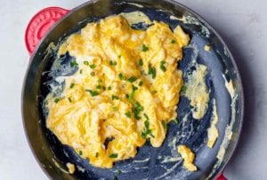 A nonstick skillet filled with scrambled eggs topped with chopped chives