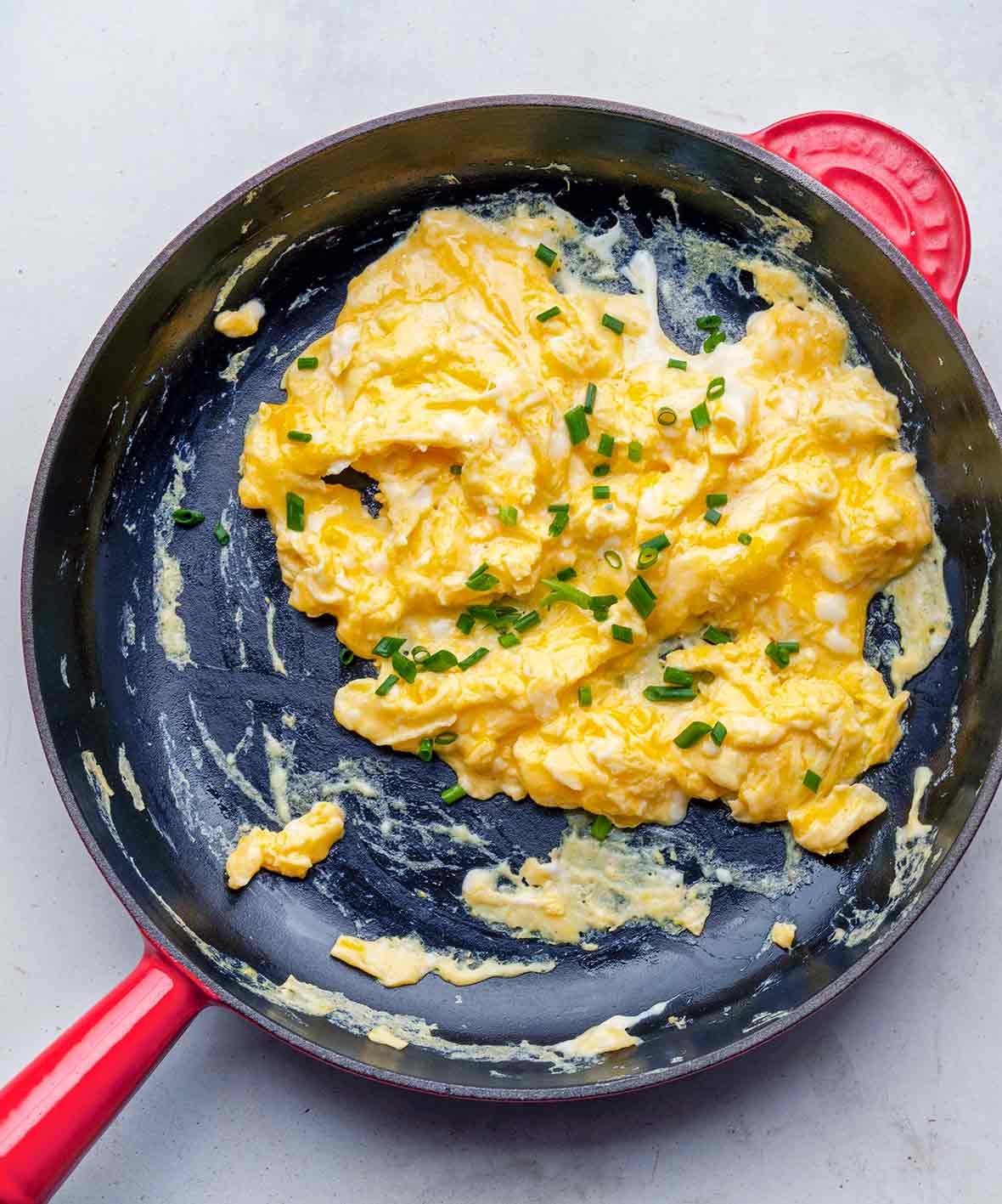 A nonstick skillet filled with scrambled eggs topped with chopped chives.