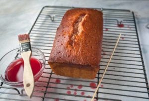 Loaf of blood orange pound cake on a wire rack with a wooden skewer.