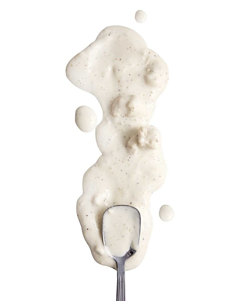 Blue cheese dip, with chunks of blue cheese, spilled in a white background with a spoon