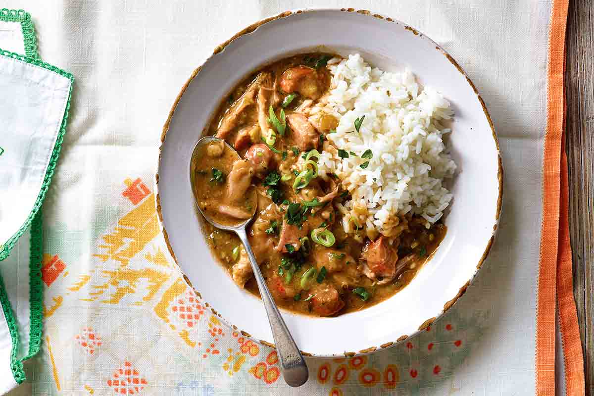 Cajun chicken and sausage gumbo with a serving of rice, in a white bowl with a spoon.