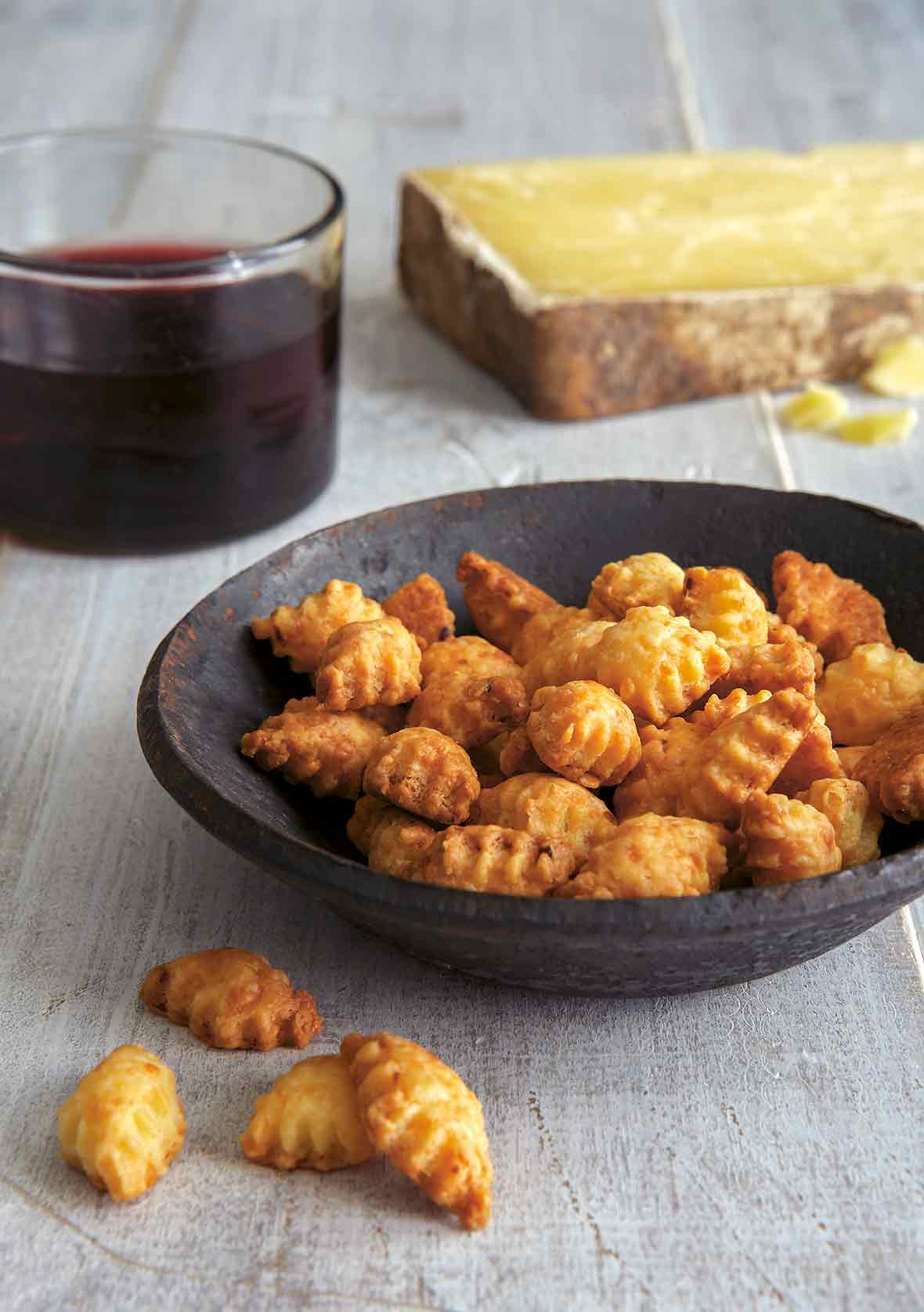 Diamond red chili and Cheddar crackers in a wooden bowl; a glass a wine and hunk of cheese