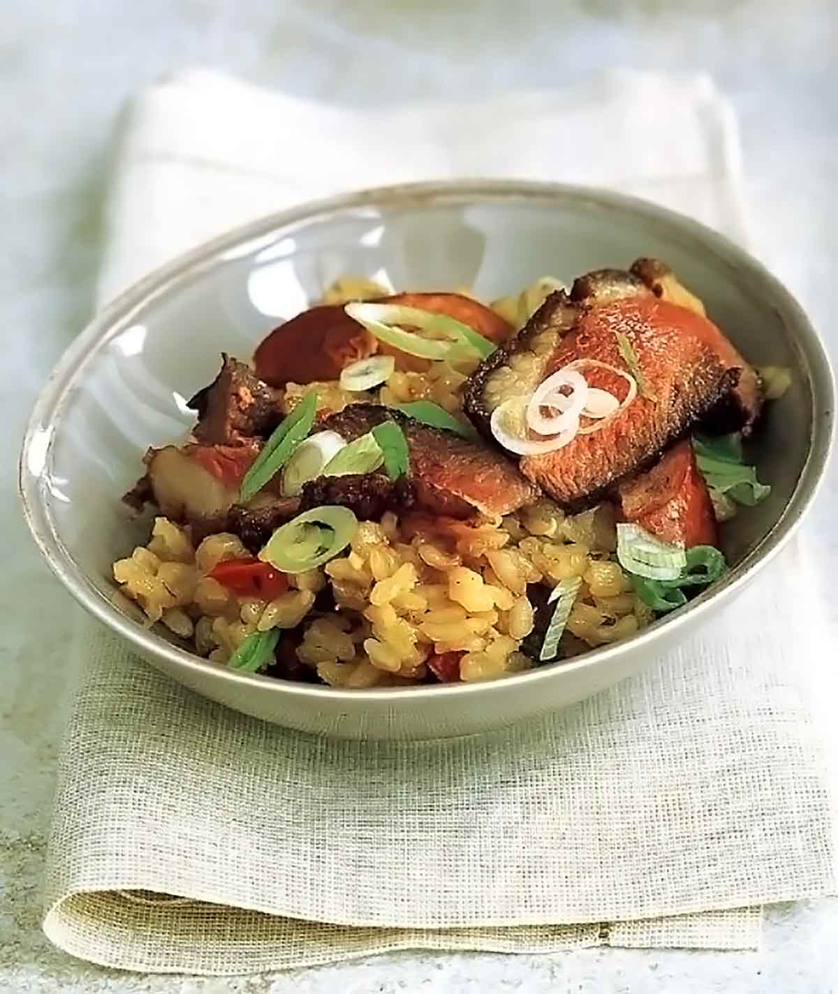 A bowl filled with duck jambalaya and topped with sausage