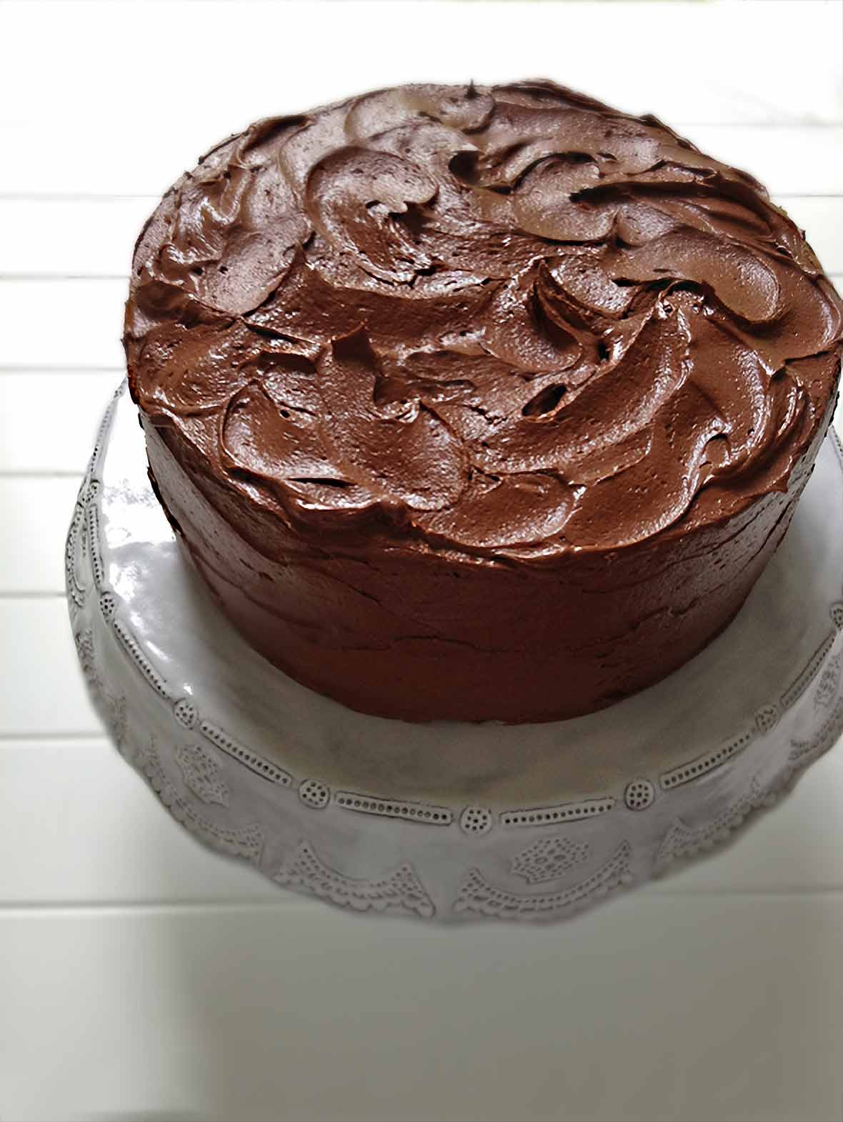 A Hershey chocolate cake with swirled chocolate frosting on a white cake stand