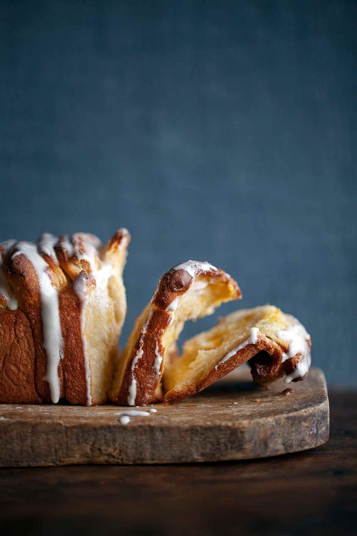 A lemon pull-apart coffee cake on a wooden board with a few slices broken off from it.