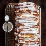 A glazed lemon pull-apart coffee cake on a wire rack with a spoon and jar of glaze beside it, all resting on a wooden cutting board.