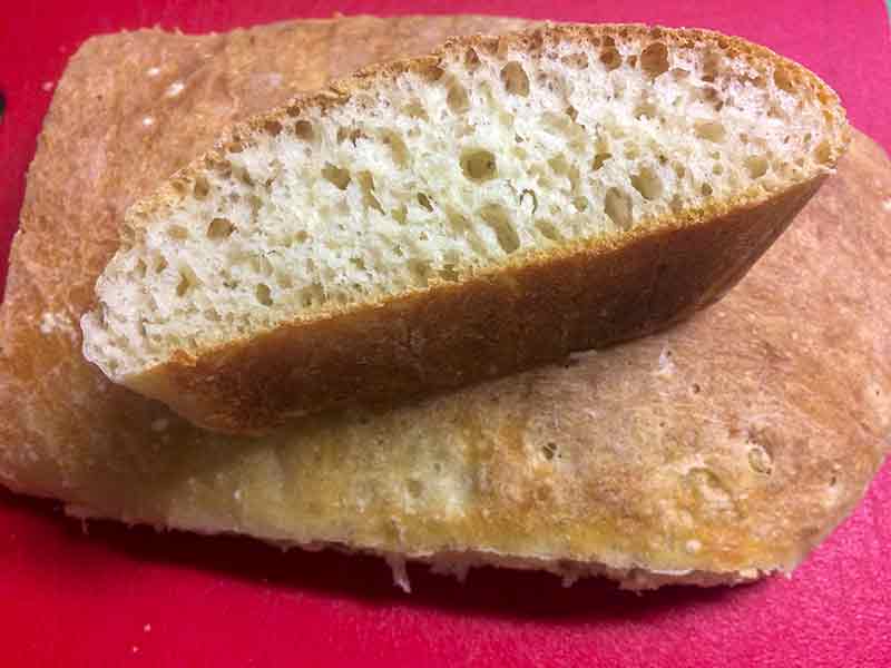 Loaf of Italian ciabatta bread sliced in half, with one half facing up to see the inside