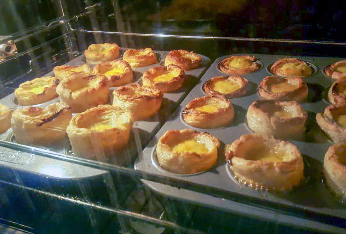 Two muffin tins in an oven filled with pasteis de nata or Portuguese custard cups