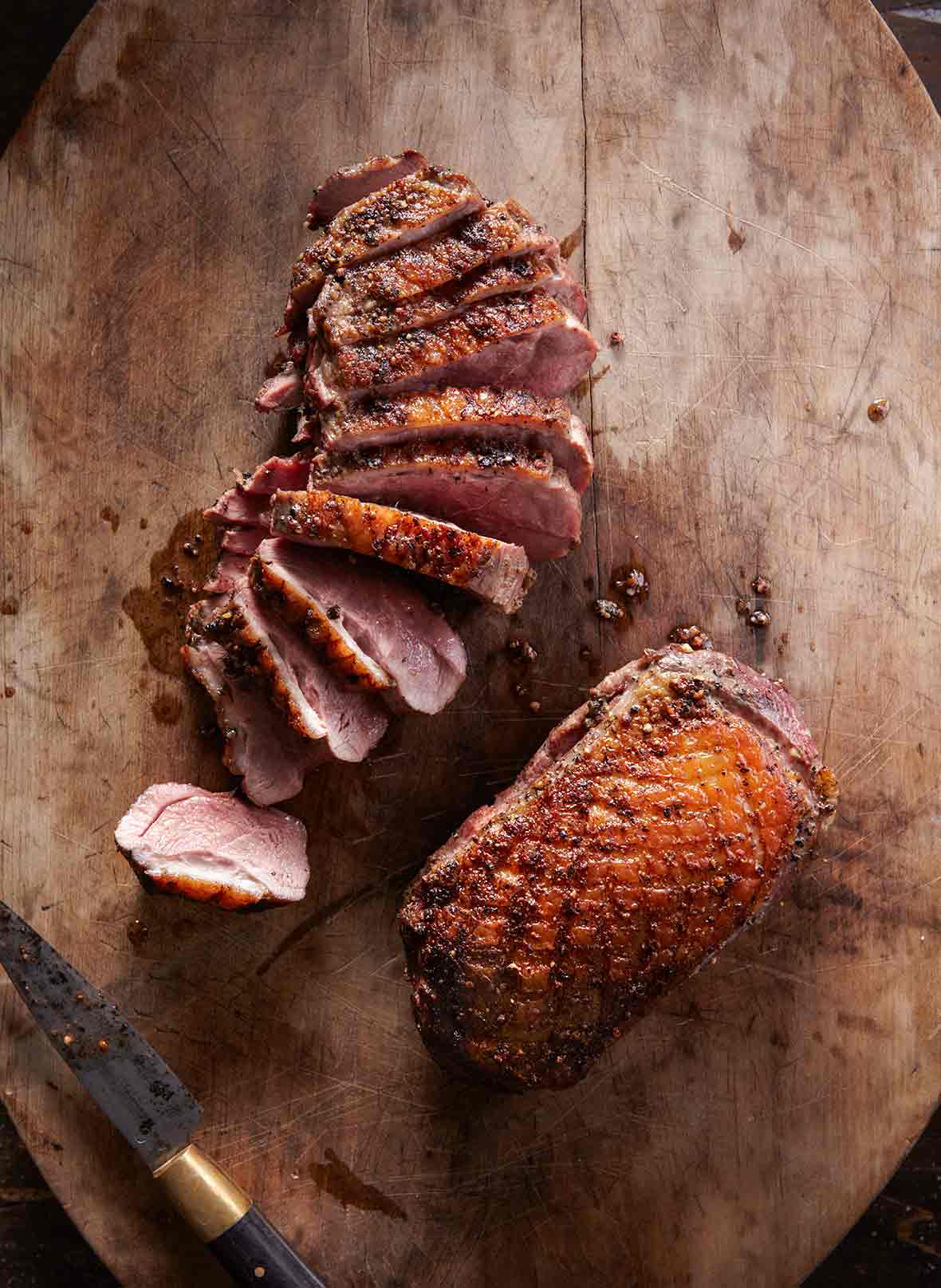 Two seared duck breasts, one sliced, the other whole on a wood cutting board
