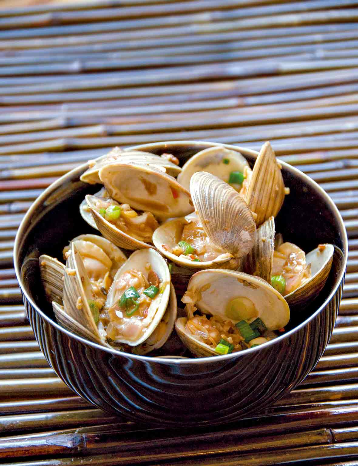 Bowl of stir-fried clams with chopped shallots, garlic, ginger, and chili flakes on bamboo