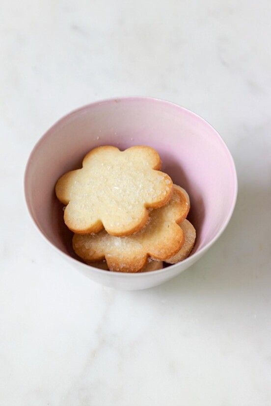 A pink bowl filled with flower-shaped sugar cookies topped with decorating sugar