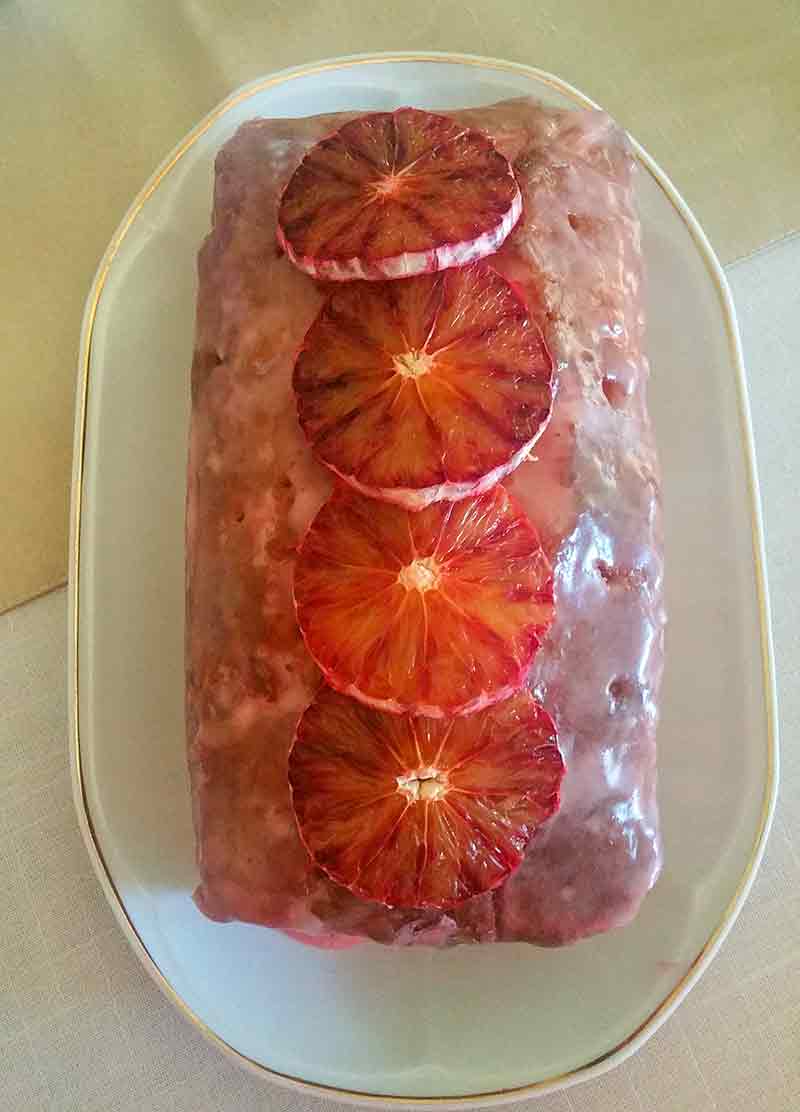 Blood orange pound cake topped with icing and four slices of blood orange in an oval plate