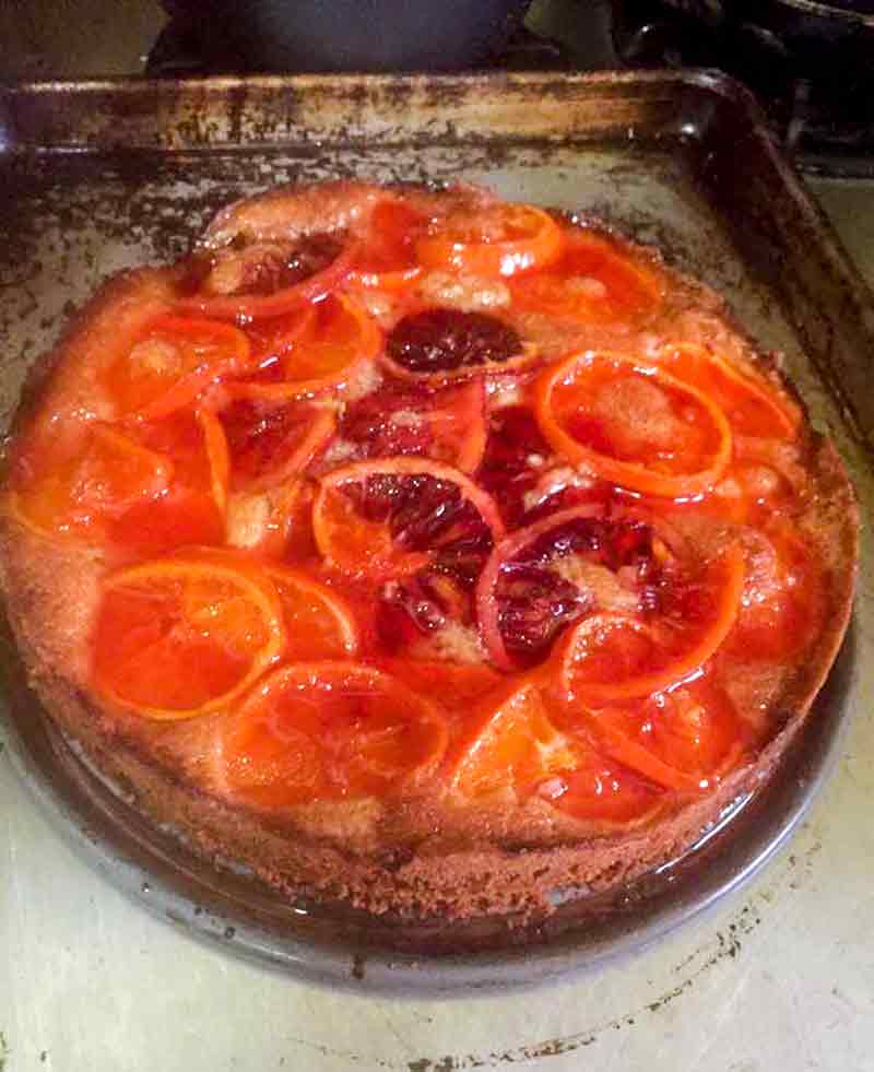 A clementine cake topped sliced oranges, blood oranges, and clementines on a baking pan