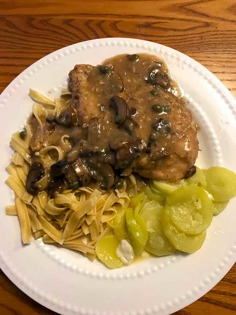 Turkey Marsala with mushrooms and parsley on top over noodles with sliced cucumber on the side