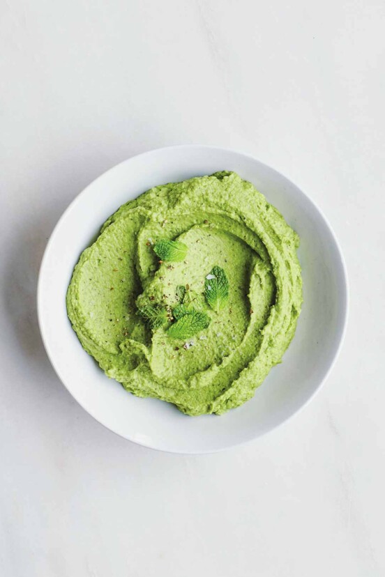 Bowl of green Spring pea puree topped with chopped mint on white marble
