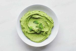 Bowl of green Spring pea puree topped with chopped mint on white marble