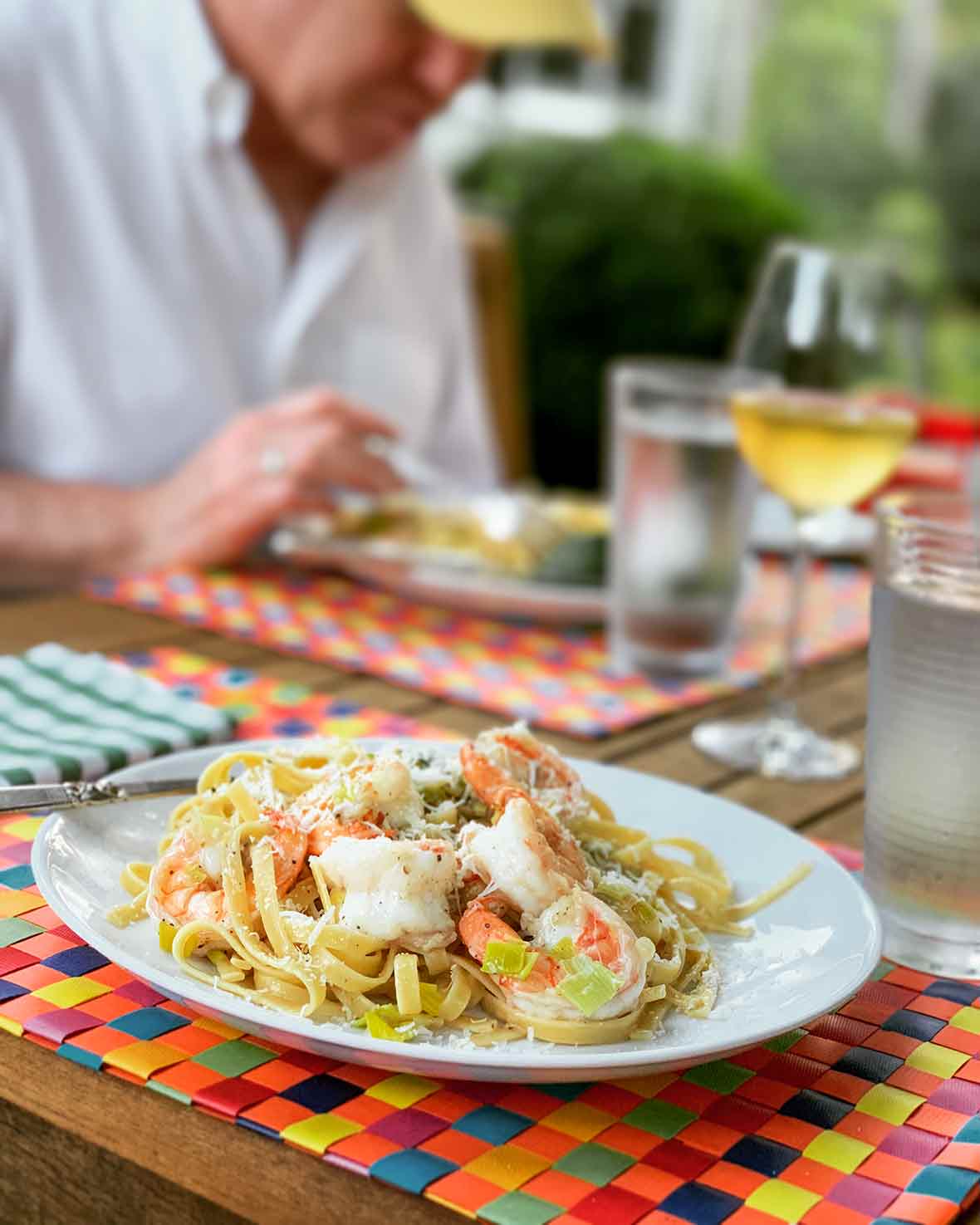 A white plate filled with shrimp and leek pasta on a multi-colored woven placemat.
