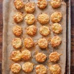 Bite-size bacon and cheese scones with smoked bacon and melted Asiago on top on a parchment-lined baking sheet.