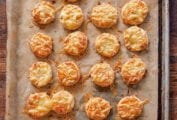 Bite-size bacon and cheese scones with smoked bacon and melted Asiago on top on a parchment-lined baking sheet.