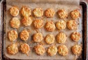 Bite-size bacon and cheese scones with smoked bacon and melted Asiago on top on a parchment-lined baking sheet